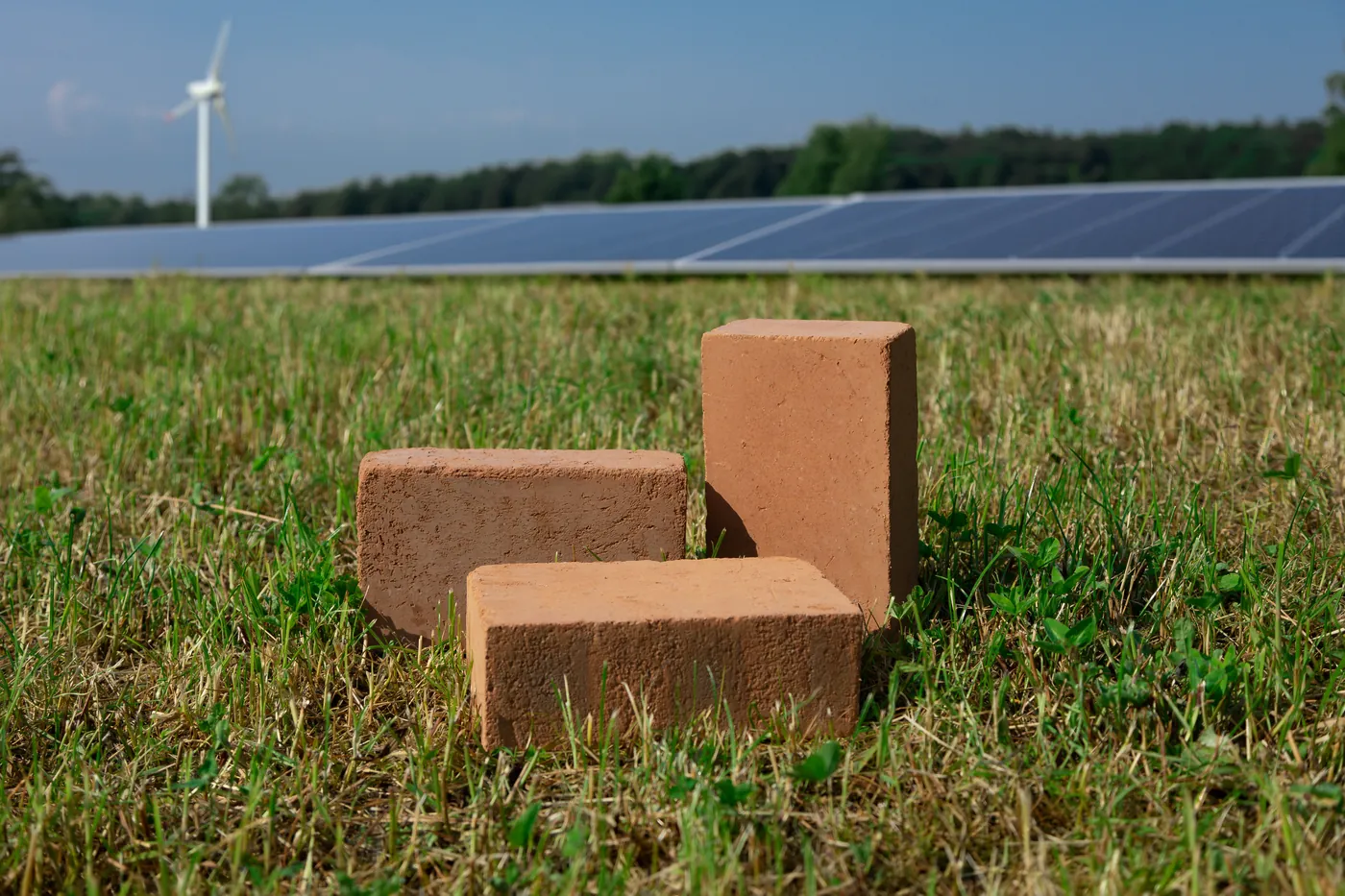 Werbefoto: drei Ziegelsteine auf einer Wiese vor Solarpark und Windrad