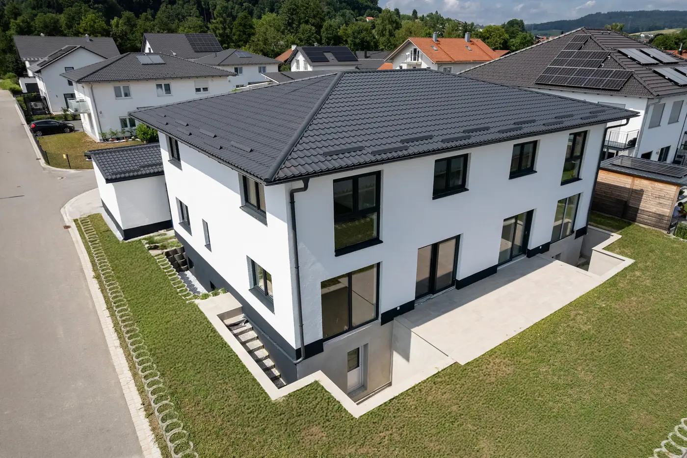 Luftaufnahme eines weißen Neubaus mit dunklem Walmdach und frisch angelegtem Rasen in einem Wohngebiet