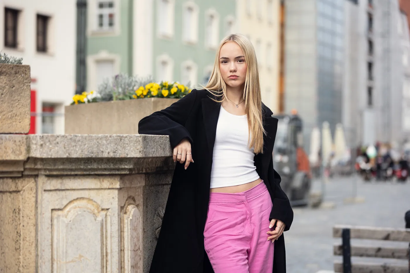 Junge Frau in schwarzem Mantel und pinker Hose in einer Altstadtgasse