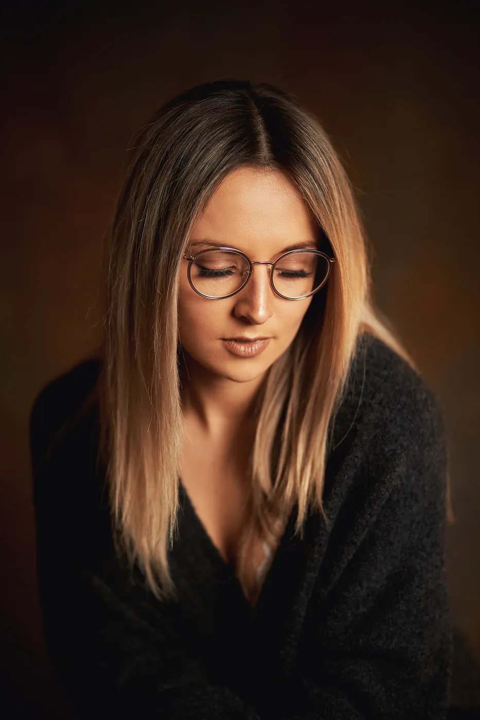 Frau mit Brille im warmen Studiolicht, Blick nach unten