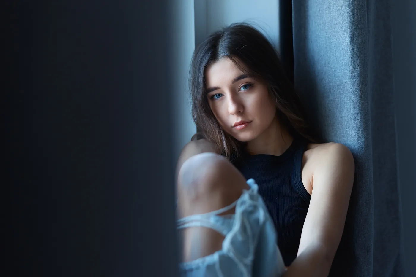 Junge Frau sitzt im Fensterlicht vor einem blauen Vorhang