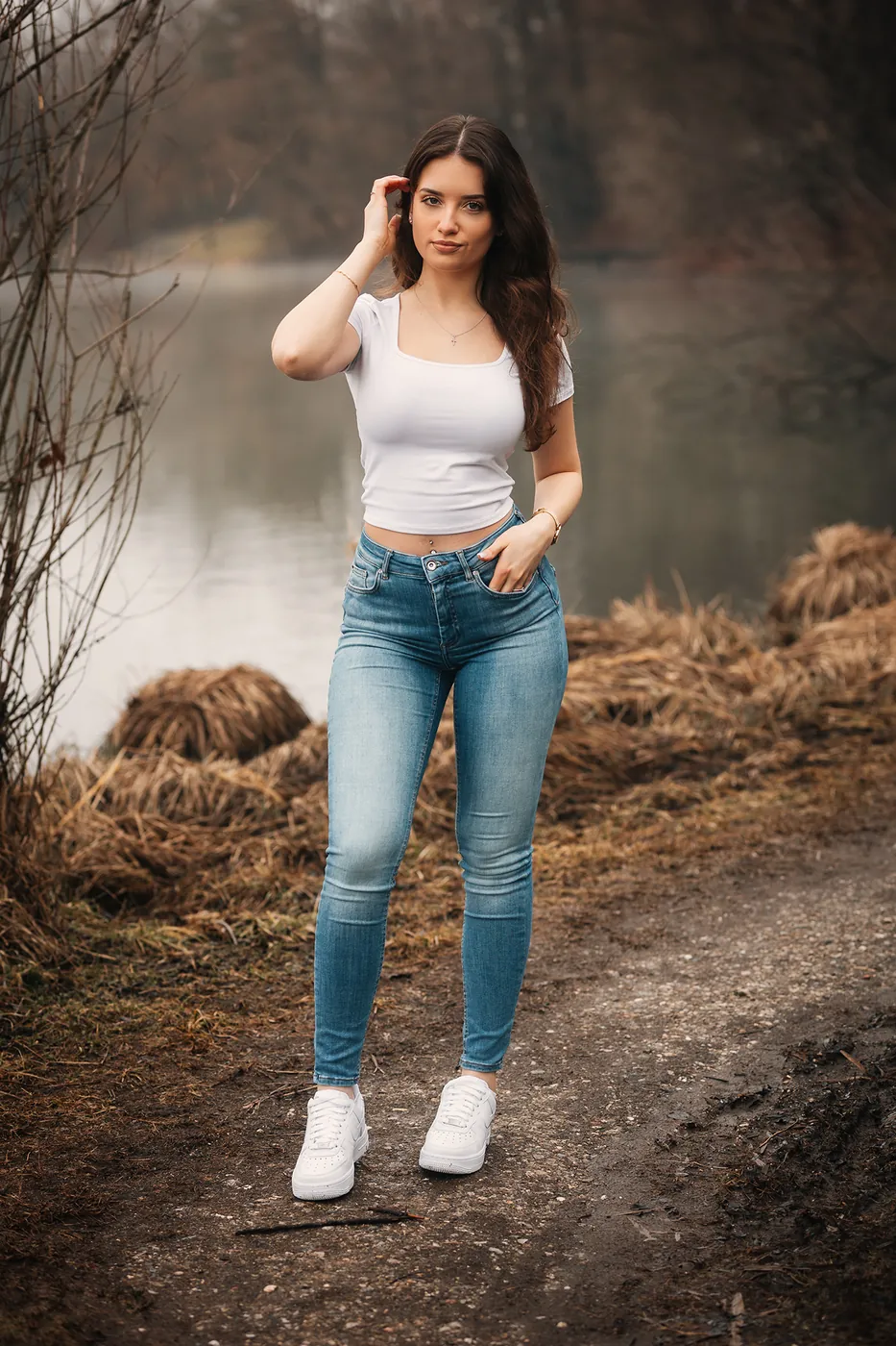 Frau in weißem Shirt und Jeans auf einem Weg am Wasser